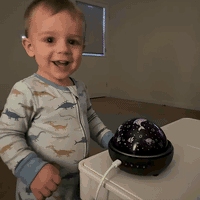 Toddler switches on the galaxy projector and the room fills with glowing dinosaur projections